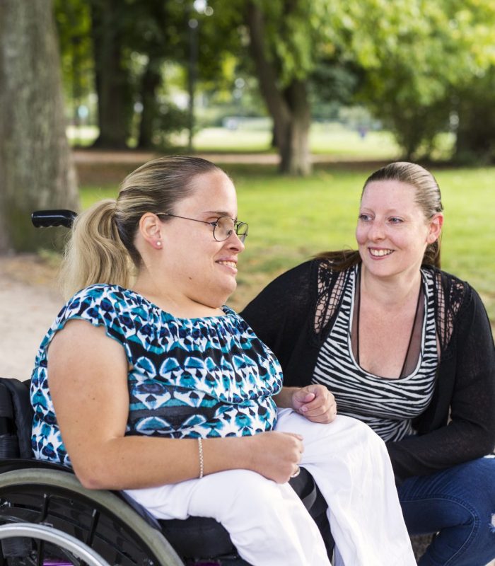 Disabled woman in wheelchair with assistant in park