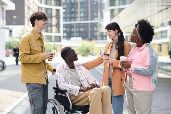Group of young friends spending time together outdoors, they drinking coffee and talking to their friend with disability