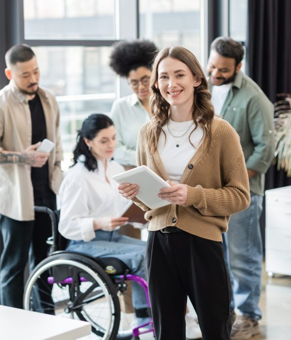 happy businesswoman with tablet near blurred interracial startup team, diversity and inclusion