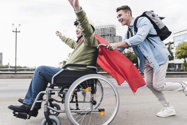 Young man pushing senior man sitting in a wheelchair dressed up as superhero